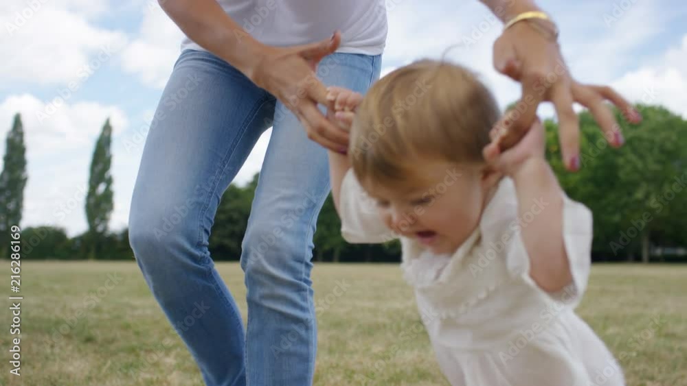 Young mother holds her daughters hands as she walks in a park, in slow motion Young mother holds her daughters hands as she walks in a park, in slow motion
