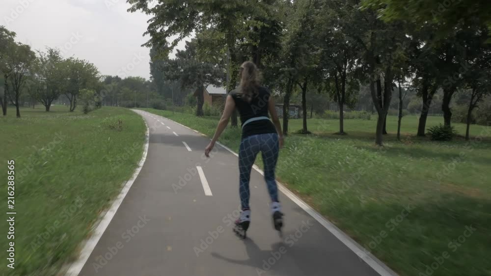 White handsom brown hair girl in tight blue pants woman riding roller skates on bike road in park, during summer day White handsom brown hair girl in tight blue pants woman riding roller skates on bike road in park, during summer day