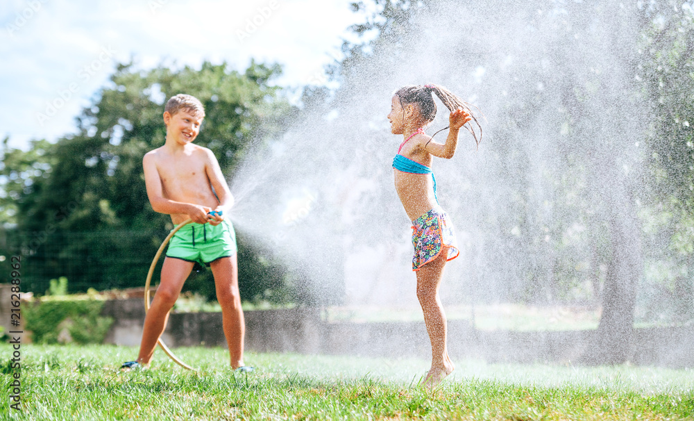 Brother and sister play together with watering hose in garden Brother and sister play together with watering hose in garden