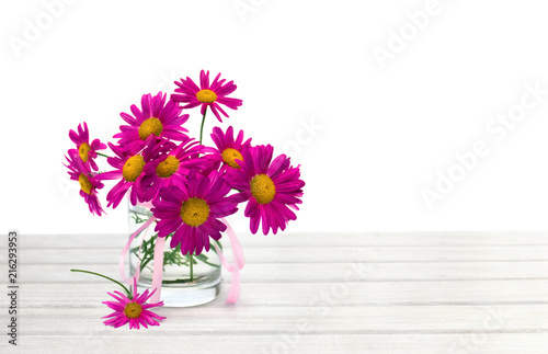 Bouquet of flowers pink daisies   Pyrethrum  Tanacetum coccineum   in small vase on white wooden table on white background with space for text