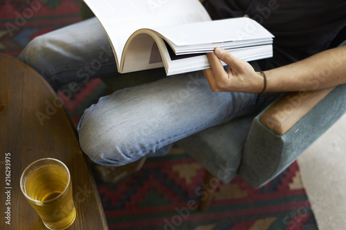 Close-up view of a man hand holding reading modern fashion magazine, glass of beer in cafe