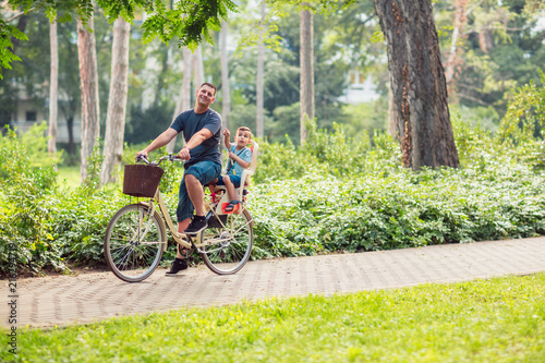 Happy family. father and son riding a bicycle together outdoors in a city park.