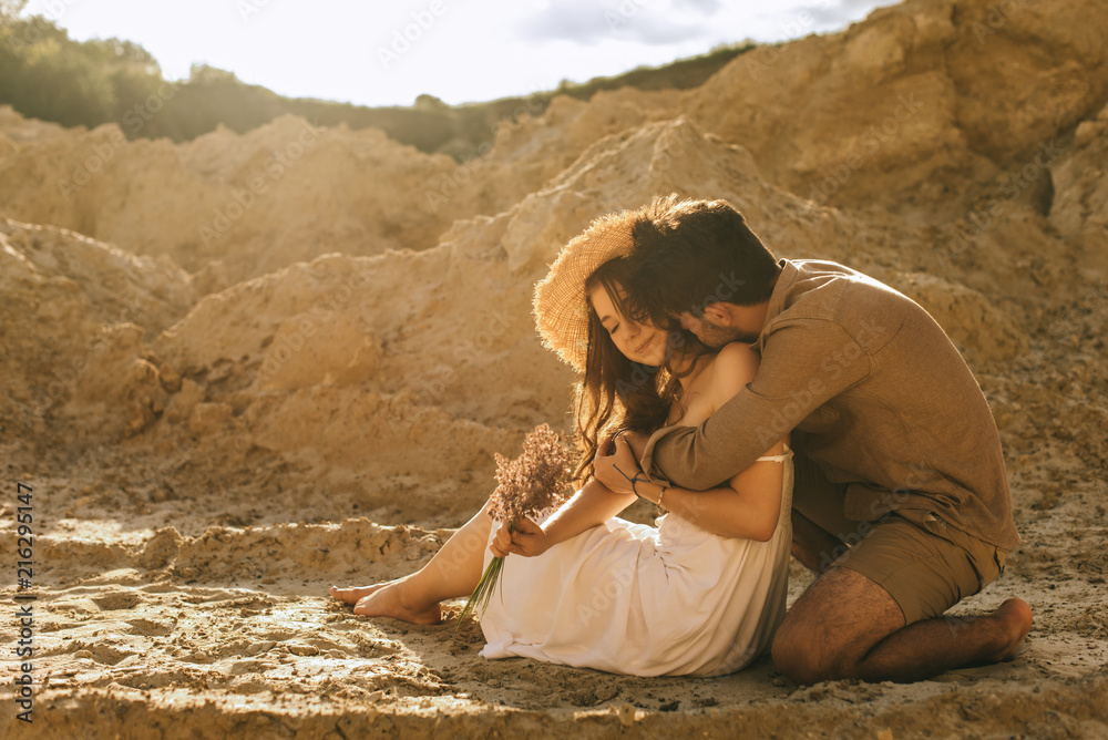 happy man hugging girlfriend in straw hat with floral bouquet in sand canyon
