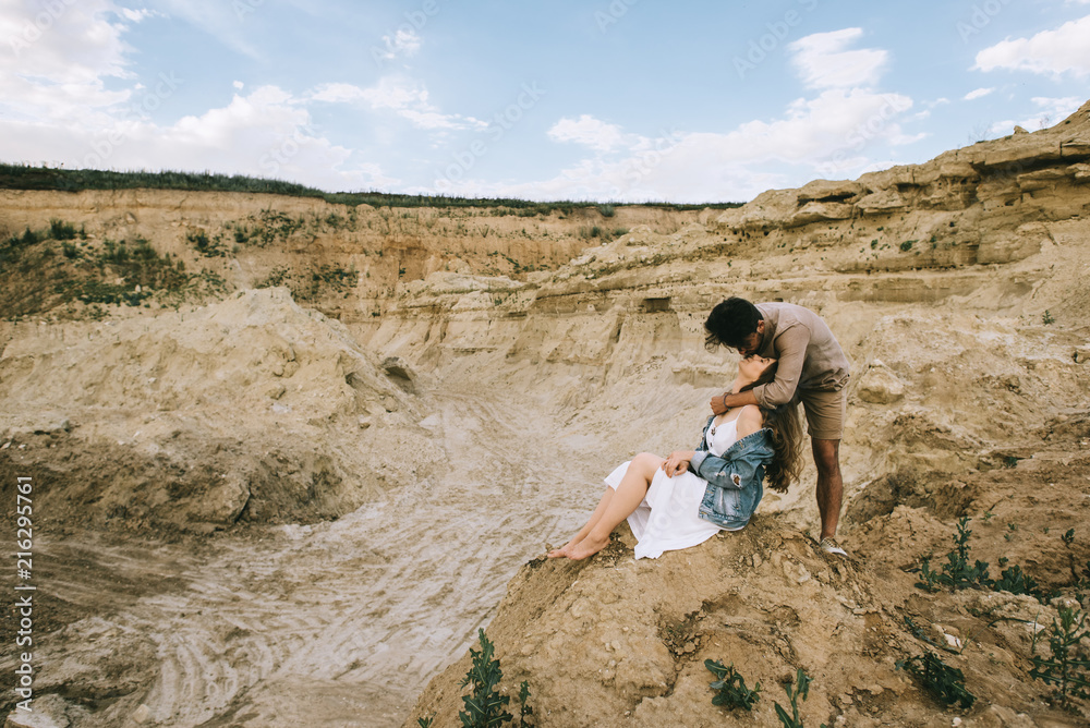 stylish man hugging and kissing girlfriend in sand canyon