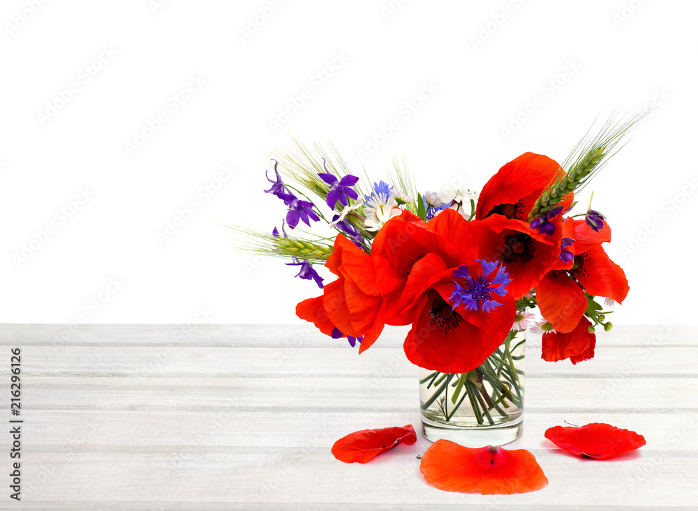 Obraz premium Red poppies, cornflowers, ears of green wheat, chamomile in small vase on white wooden table on white background with space for text.