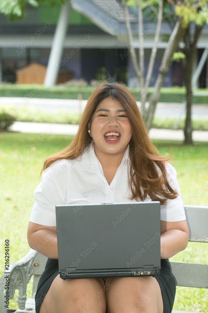 Portrait of pretty smiley face Asian fat woman pose working with laptop on a chair in the park. Portrait of pretty smiley face Asian fat woman pose working with laptop on a chair in the park.