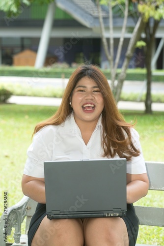 Portrait of pretty smiley face Asian fat woman pose working with laptop on a chair in the park.
