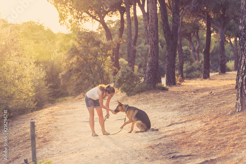 Young attractive latin woman walking with her beautiful cute german shepherd dog in the park at sunset in summer in nature care support happiness family peaceful friendship animals lifestyle concept.