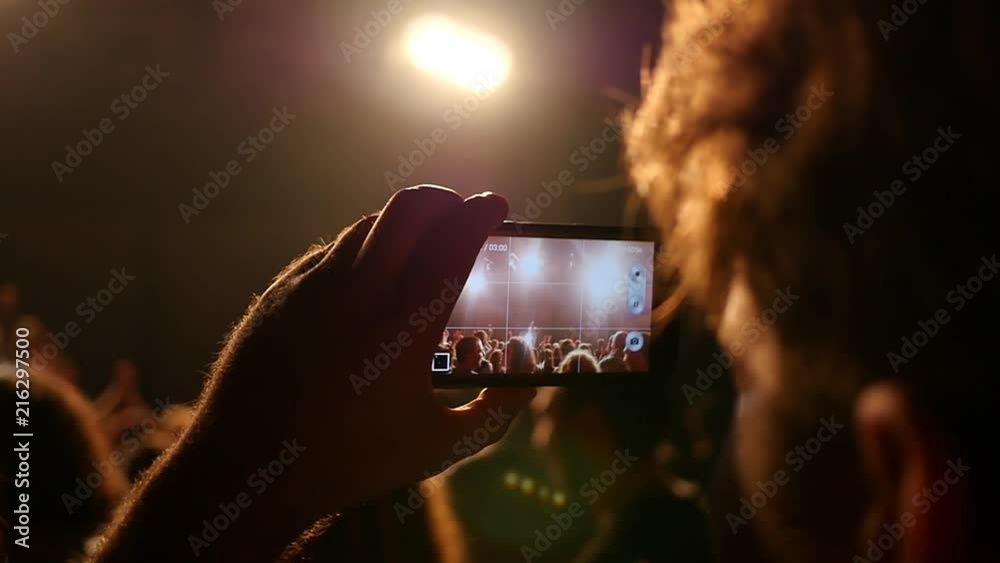 Spectator fan shooting video via smart phone at a music concert lumiere