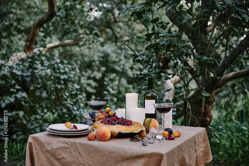tasty appetizing berries pie, red wine and candles on table in garden © LIGHTFIELD STUDIOS