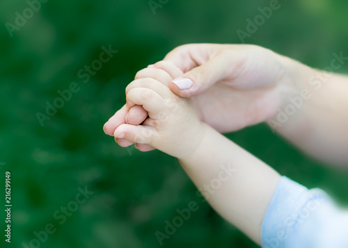 Mother holding hand of newborn baby on green grass background. The concept of maternal tenderness, care and health. © tanya69