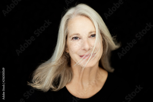 stunning beautiful and self confident best aged woman with grey hair smiling into camera, portrait with black background