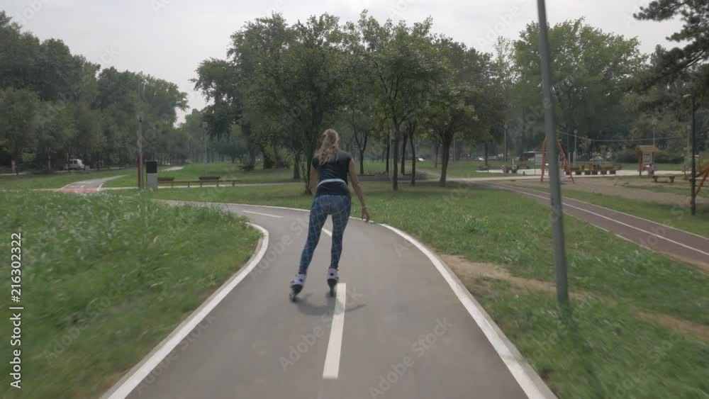 White handsom brown hair girl in tight blue pants woman riding roller skates on bike road in park, during summer day White handsom brown hair girl in tight blue pants woman riding roller skates on bike road in park, during summer day