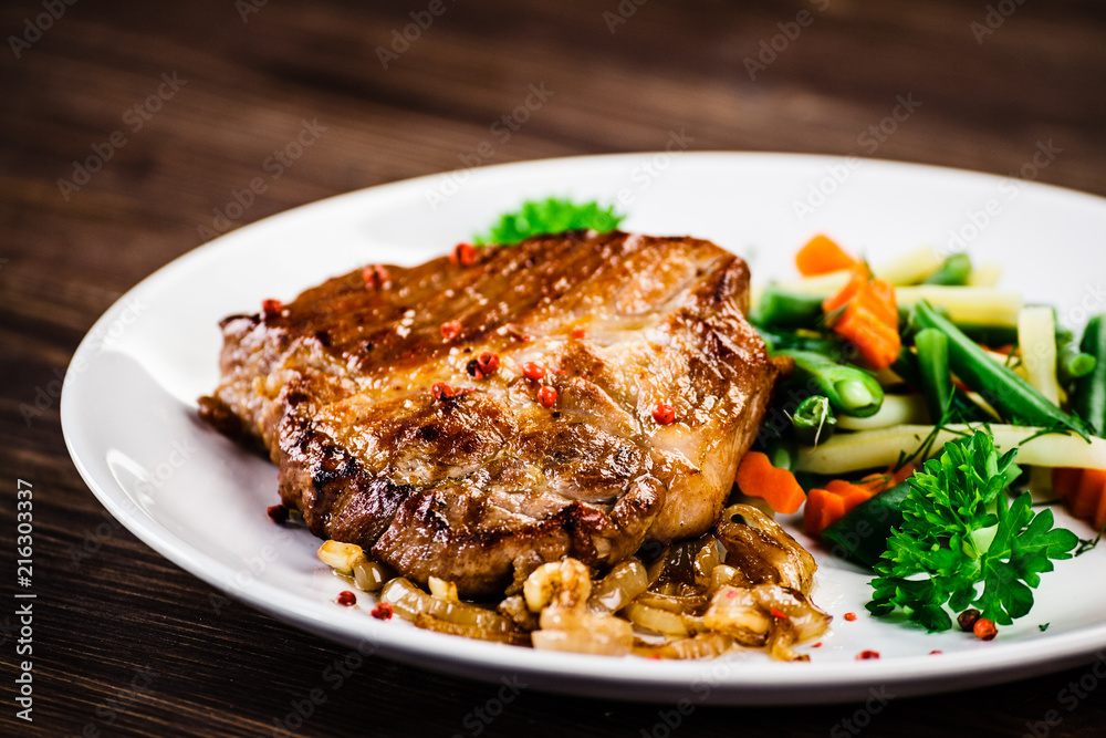 Grilled steak with vegetables on wooden background