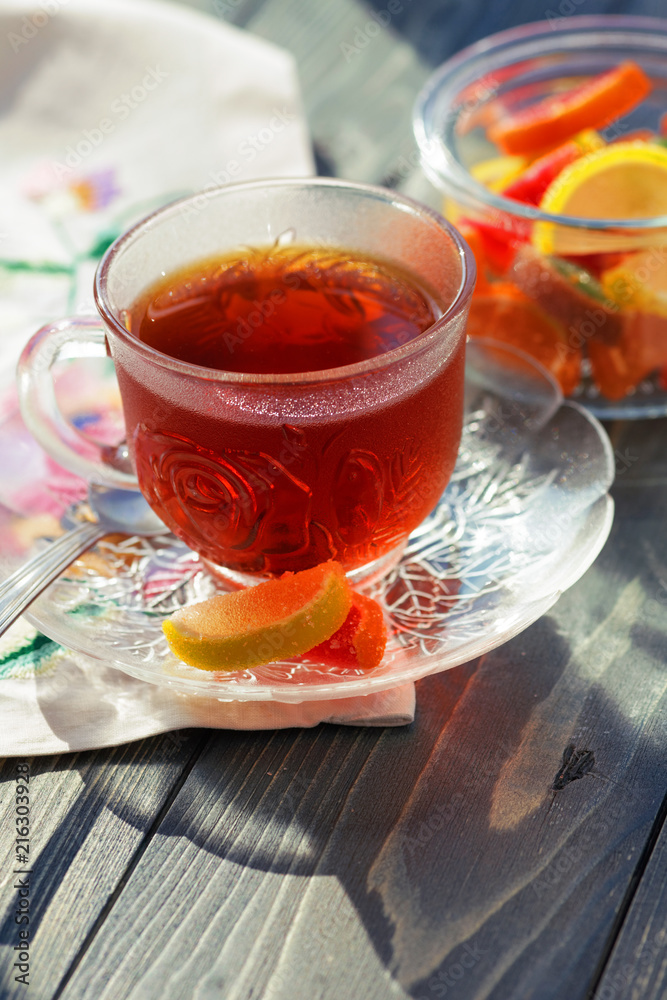 Close up of a morning black tea and colorful marmalades in glass jar on wooden table Close up of a morning black tea and colorful marmalades in glass jar on wooden table