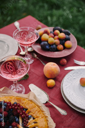 berries pie, fruits and glasses of wine on table in garden