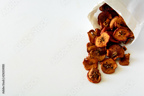 Tasty apple chips wrapped in paper on white wooden background