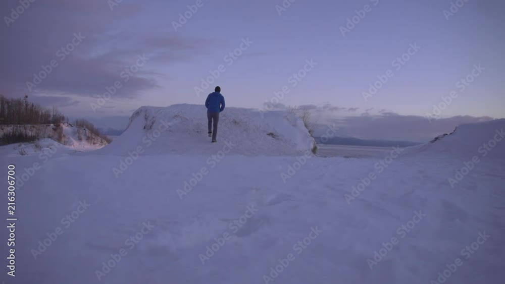 Man in blue walking/running on snowy road in winter. Cold scene. Taking in the view. Shot in Alaska. Man in blue walking/running on snowy road in winter. Cold scene. Taking in the view. Shot in Alaska.