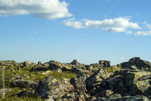 rocky grassy terrain on a mountain pass and a blue sky with clouds above it © Evgeny