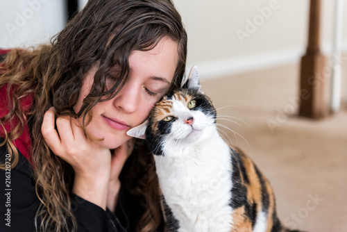 Fotografia Young woman bonding with calico cat bumping rubbing bunting heads, friends frien