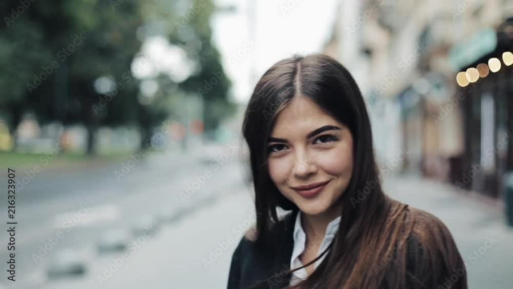Young business woman walks down the central city street, turns and smiles right to the camera, posing and playing with her long hair. Being emotional, cheerful mood Young business woman walks down the central city street, turns and smiles right to the camera, posing and playing with her long hair. Being emotional, cheerful mood