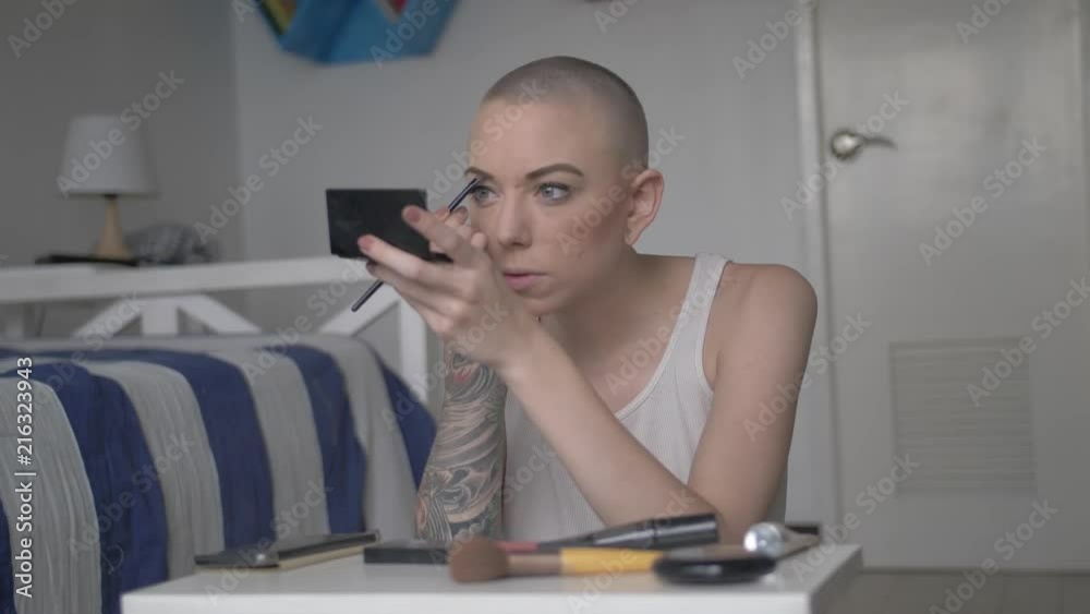 A pretty woman with short hair and tattoos carefully applies makeup to her eyes while sitting on the floor. Slow motion. A pretty woman with short hair and tattoos carefully applies makeup to her eyes while sitting on the floor. Slow motion.