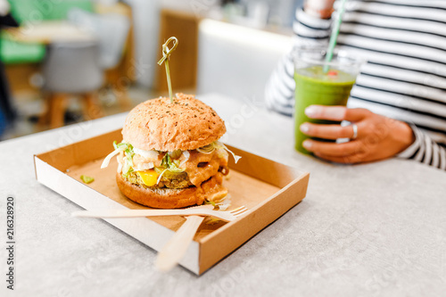 A young woman drinks green smoothies and eats a burger in a vegan fast food restaurant