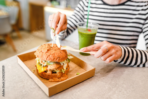 A young woman drinks green smoothies and eats a burger in a vegan fast food restaurant photo