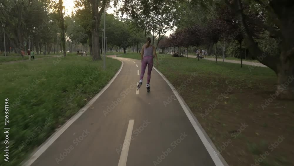 White hansom brown hair girl in tight violet pants woman riding roller skates on bike road in park, during summer golden hour White hansom brown hair girl in tight violet pants woman riding roller skates on bike road in park, during summer golden hour