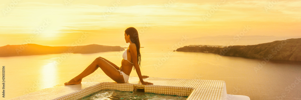 Luxury travel Santorini hotel woman by resort swimming pool at sunset - Bikini body model sunbathing banner panorama. - obrazy, fototapety, plakaty 