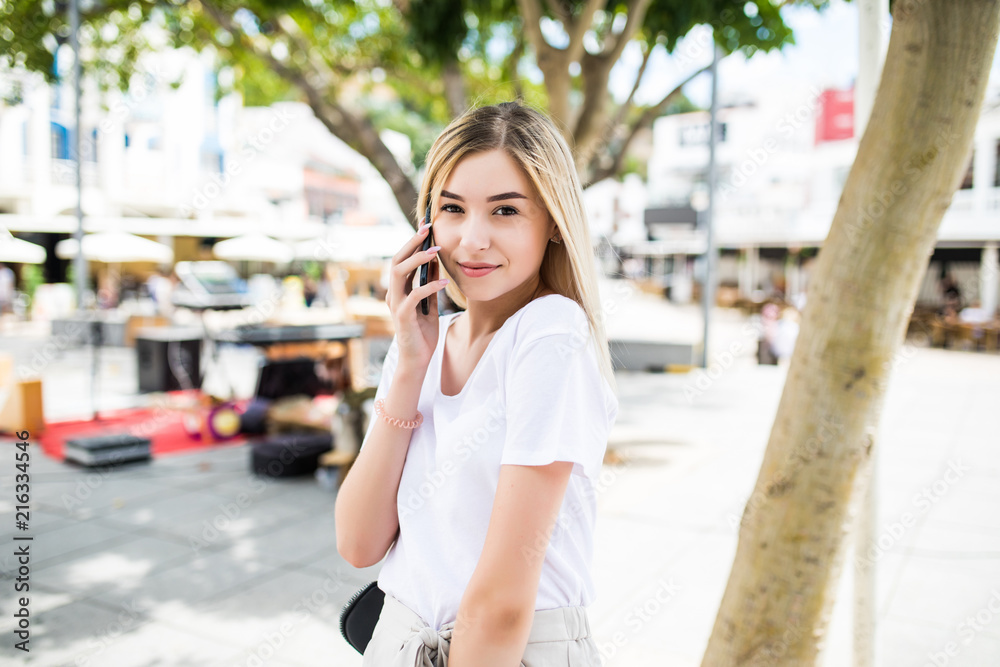 Happy young woman talking on phone at city street lifestyle portrait in the summer time