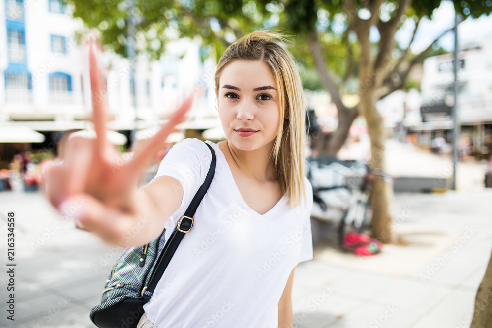 Portrait of a cheerful woman. Lovely woman showing victory or peace sign outdoors in summer street.
