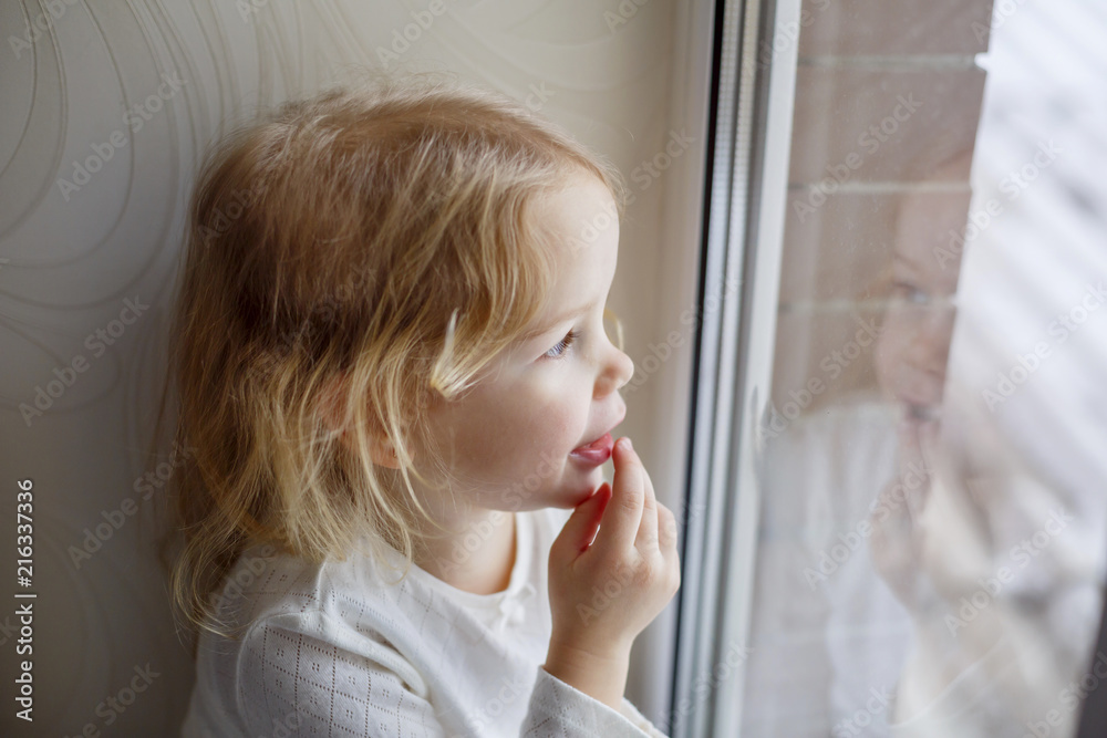 Little girl sitting on windowsill and looking out window Little girl sitting on windowsill and looking out window
