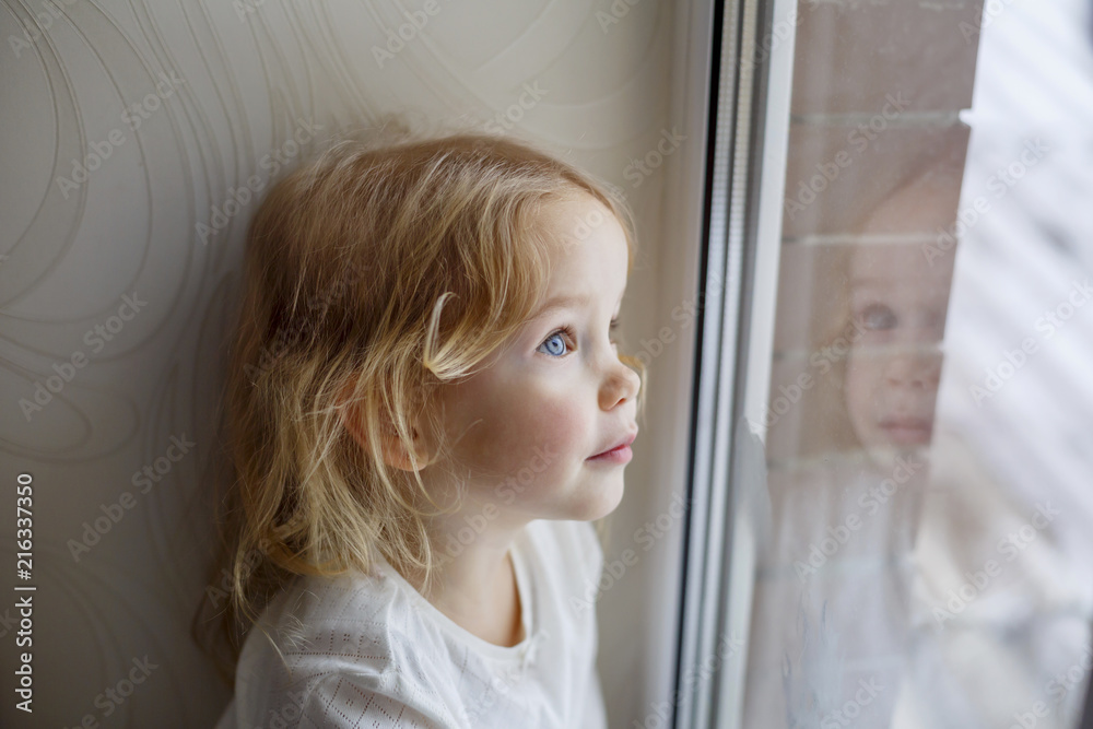 Little girl sitting on windowsill and looking out window Little girl sitting on windowsill and looking out window