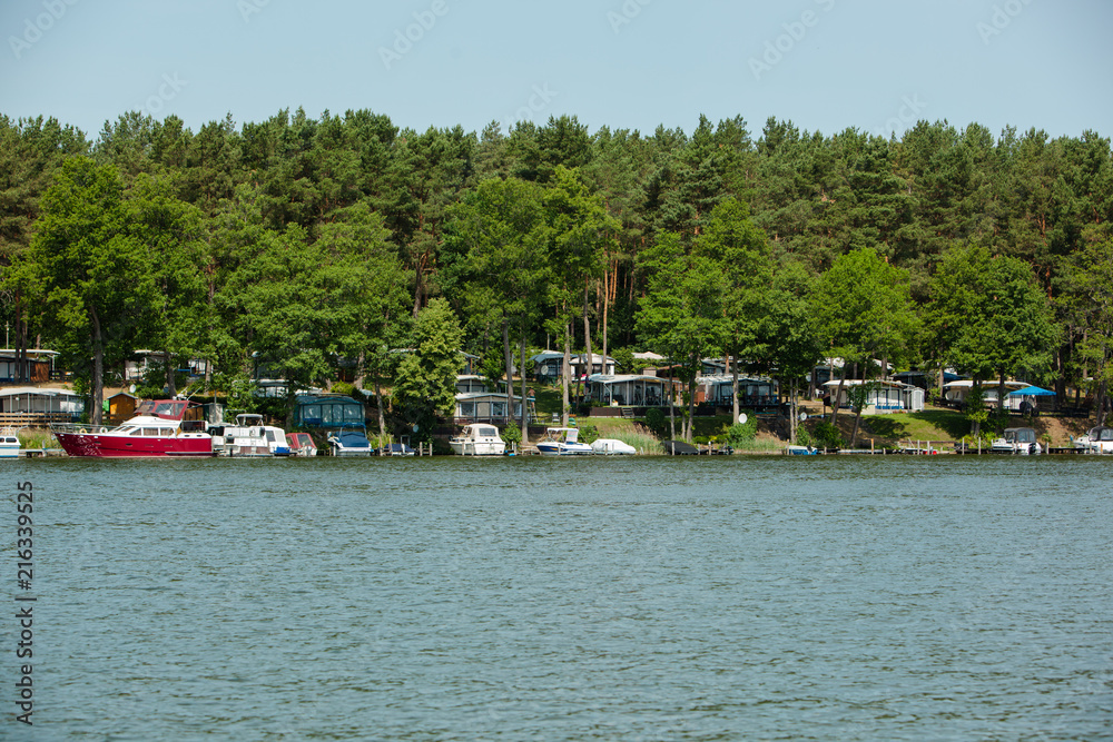 Camping Site with private Boats situated under Trees on a Lake on a sunny Day