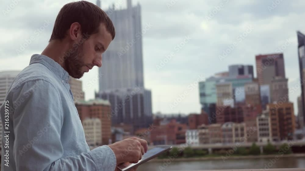 A man uses a tablet in downtown area with cinematic skyscrapers A man uses a tablet in downtown area with cinematic skyscrapers