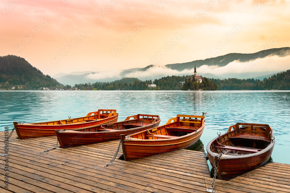 Boats on Bled Lake in Slovenia. Mountain lake with small island, church and colorful sky, stylized sunrise.