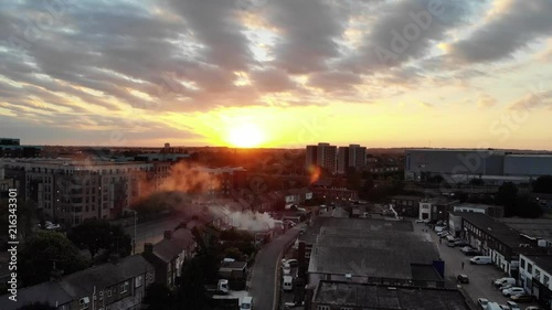 Drone raising up revealing downtown Romford as seen through the chimney smoke illuminated by sunrays at sunset photo