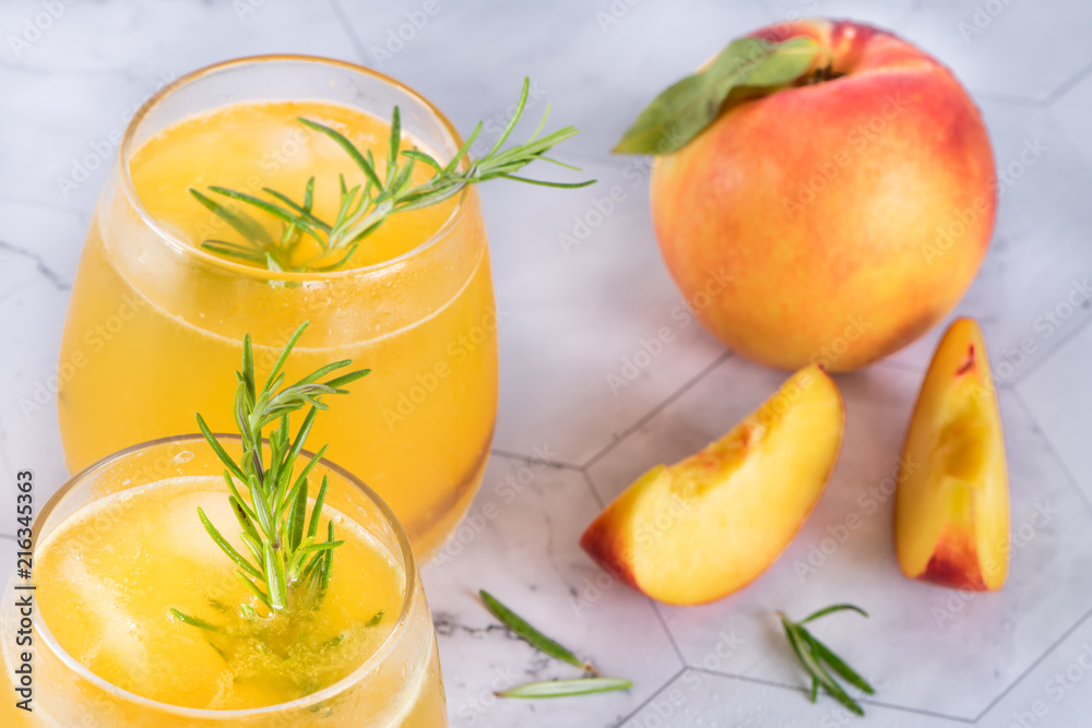 Homemade peach juice with ice cubes and rosemary leaves in glass on marble stone background. Homemade peach juice with ice cubes and rosemary leaves in glass on marble stone background.