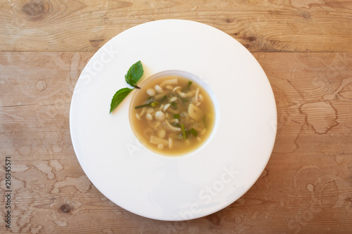 Mushroom garlic chive broth in white bowl garnished with basil, old wood background, horizontal aspect