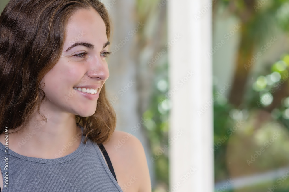 Young woman smiles at something happening outside through window with room for text
