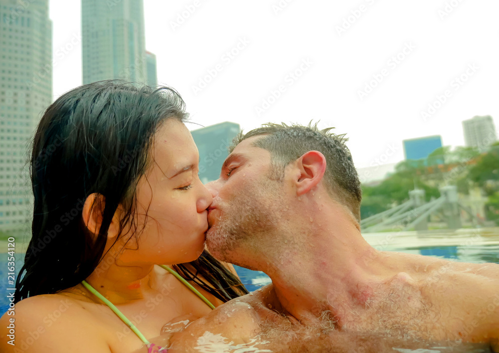 young happy and attractive playful couple taking selfie picture together with mobile phone at luxury urban hotel kissing at infinity pool enjoying holidays