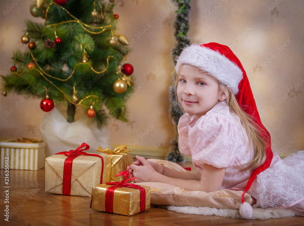 Girl in Santa hat dreaming under Christmas tree with gifts