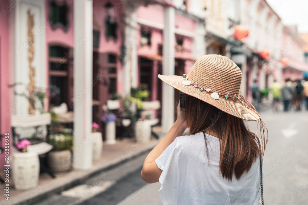 Young woman traveler walking and taking a photo at Phuket old town in Thailand