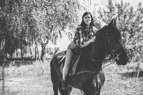 Woman enjoying horse company. Young Beautiful Woman dressed plaid shirt With black Horse Outdoors, stylish girl at american country style 