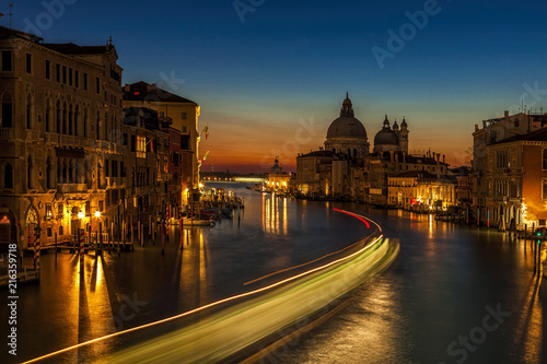 Long exposure of a vaporetto traveling up the Grand Canal towards the Santa Maria della Salute church as seen from the Accademia Bridge