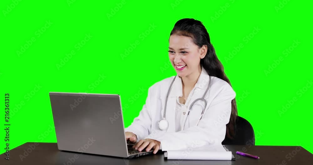 Beautiful female doctor working with a laptop computer on the table, shot with green screen background Beautiful female doctor working with a laptop computer on the table, shot with green screen background