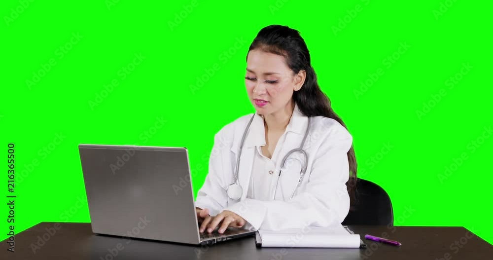 Young female doctor using a laptop computer on the table and smiling at the camera with green screen background. Shot in 4k resolution Young female doctor using a laptop computer on the table and smiling at the camera with green screen background. Shot in 4k resolution