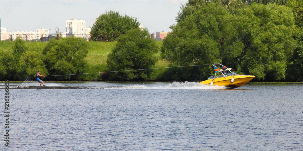 Yellow wakeboard boat with rider in Moscow river on the background of green shore - outdoor activities on the river, water skiing, wakeboard, summer, sports,