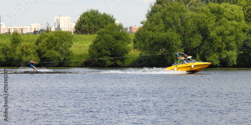 Obraz na płótnie Yellow wakeboard boat with rider in Moscow river on the background of green shore - outdoor activities on the river, water skiing, wakeboard, summer, sports, w salonie
